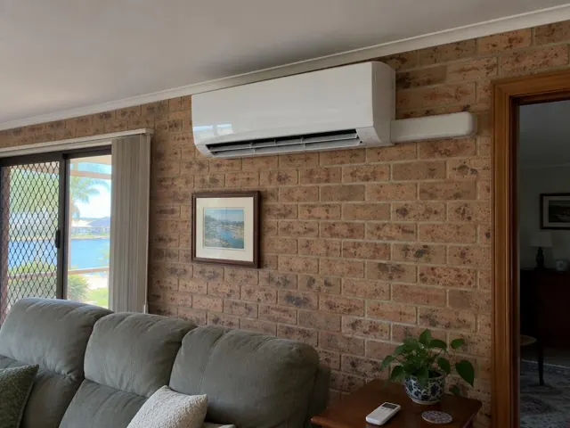 Running split system on a brick living room wall above a sofa, with louvre open in Runaway Bay