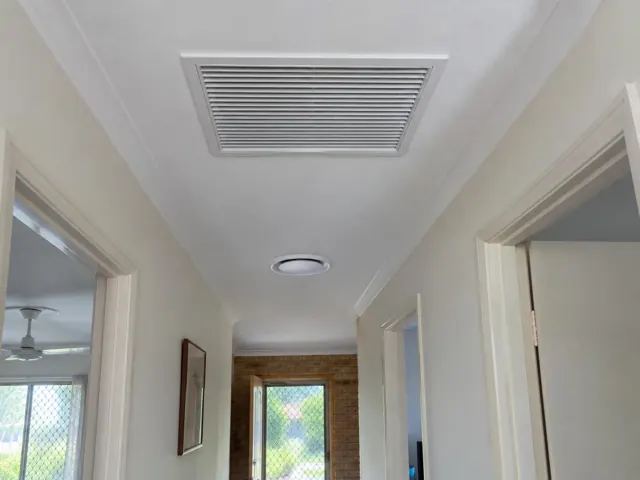 Ceiling return-air grille and round outlet in a narrow home hallway with white walls and doorways in Biggera Waters